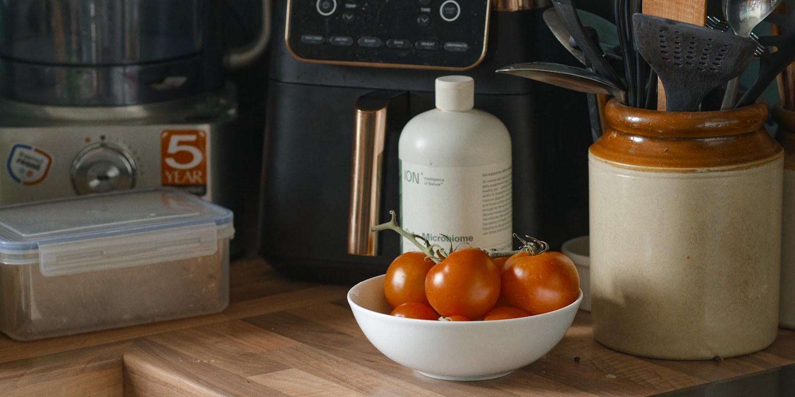 An air fryer on a wooden kitchen worktop beside a bowl of tomatoes - the best air fryer under £100 needs to earn that space