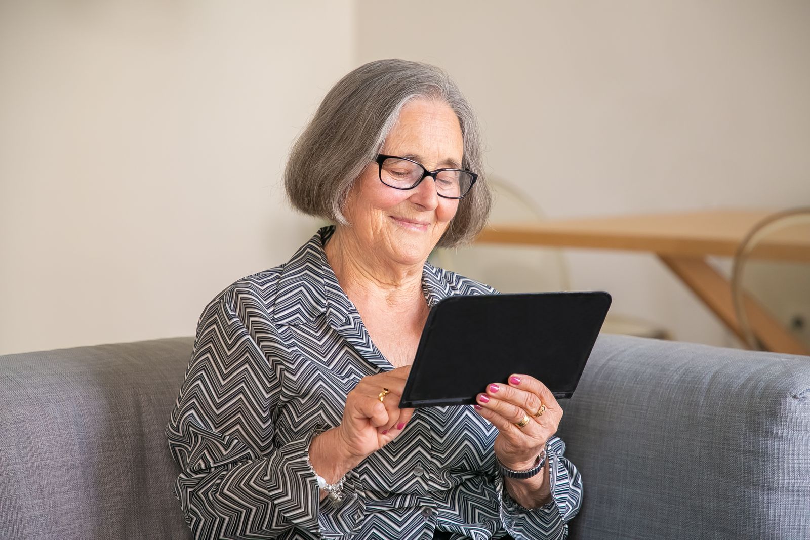Elderly woman looking at photos on a tablet screen with a cup of tea