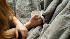 Best electric blanket 2026: woman wrapped in a warm blanket holding a mug on a cold evening