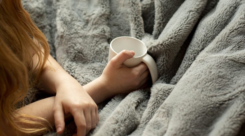 Best electric blanket 2026: woman wrapped in a warm blanket holding a mug on a cold evening