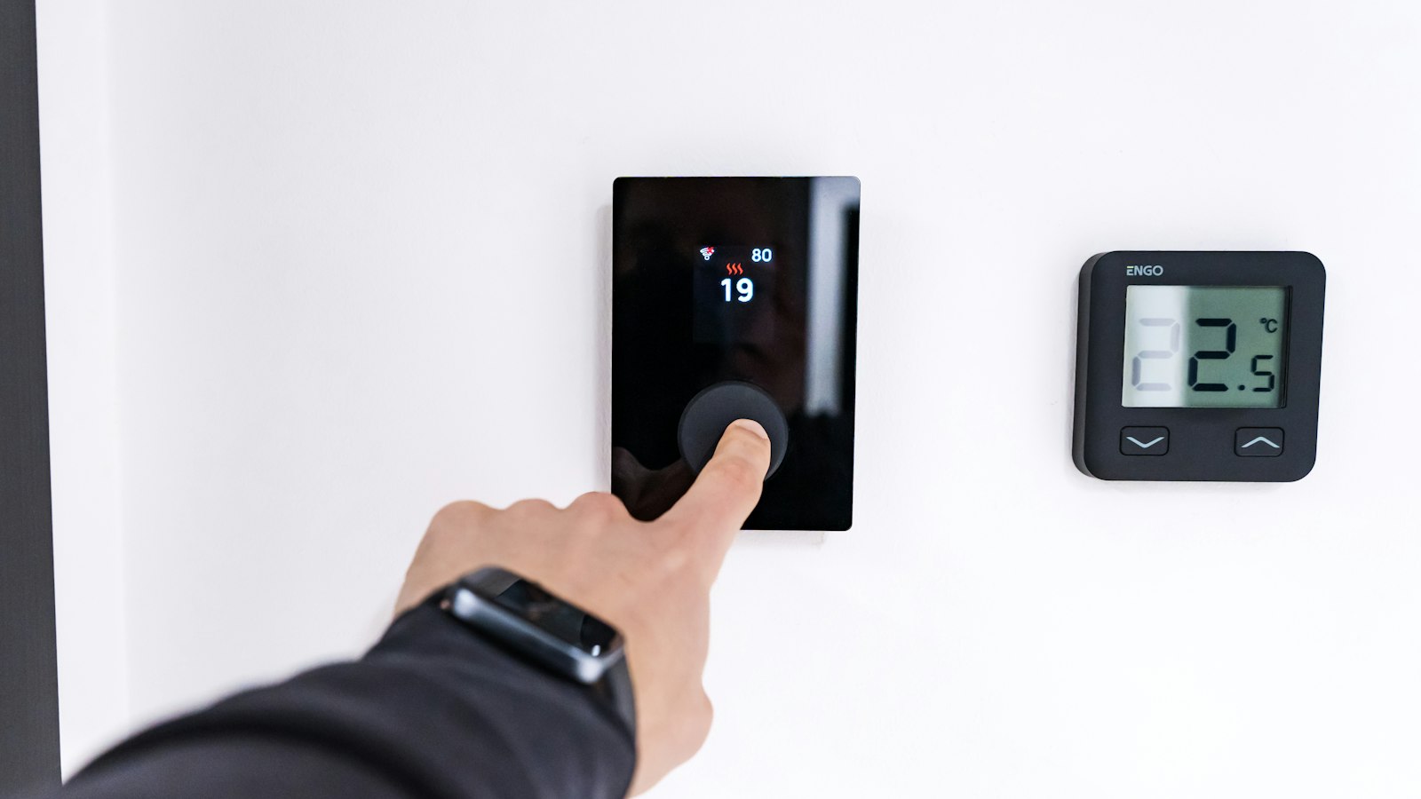 Finger adjusting a wall-mounted digital thermostat, the kind a best smart thermostat under £150 replaces