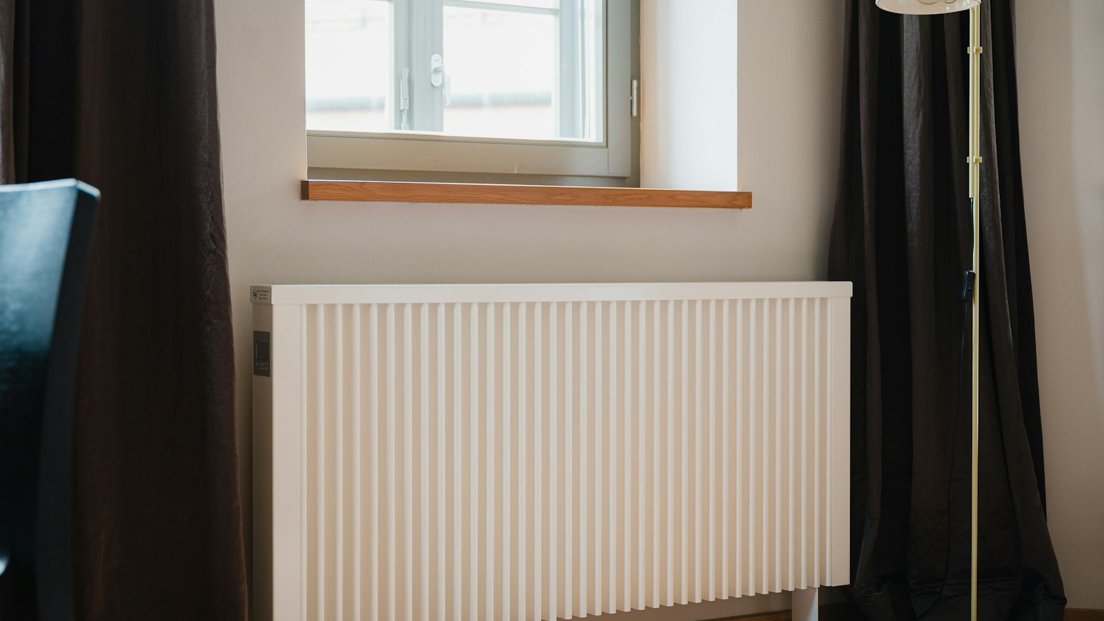 White panel radiator in a bright room, the kind of central heating a smart thermostat controls