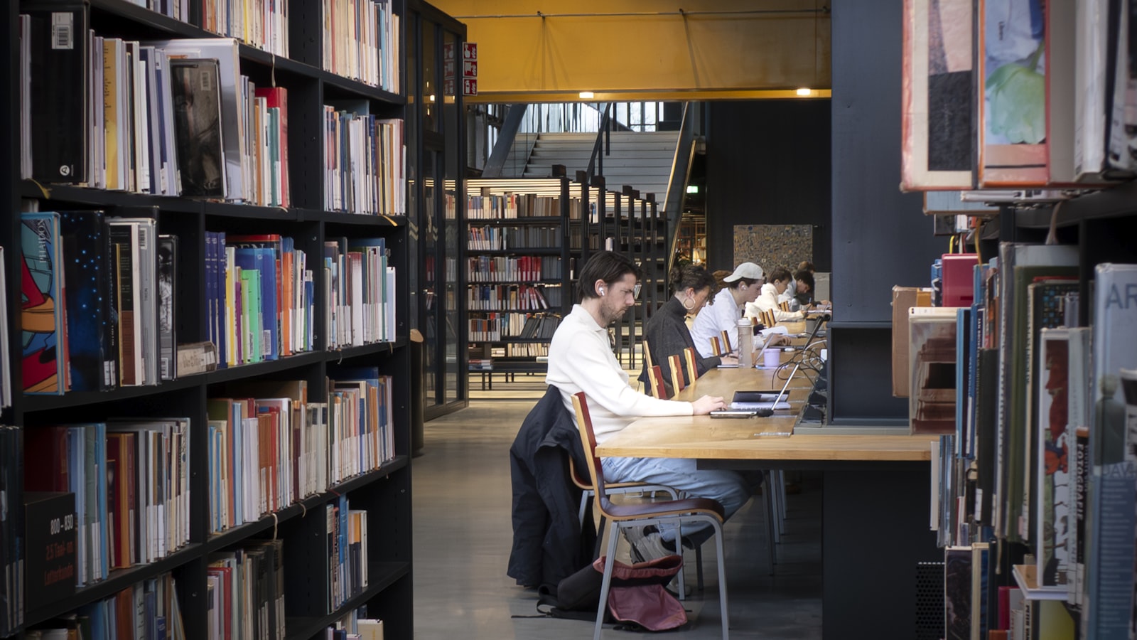 Students working on laptops at tables in a modern university library