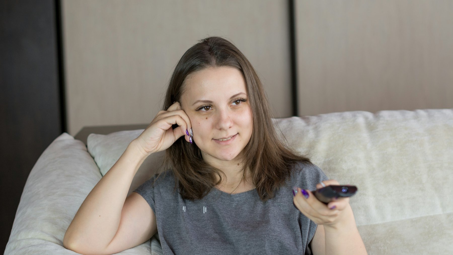 Woman on a sofa with a remote control, watching television at home in the evening