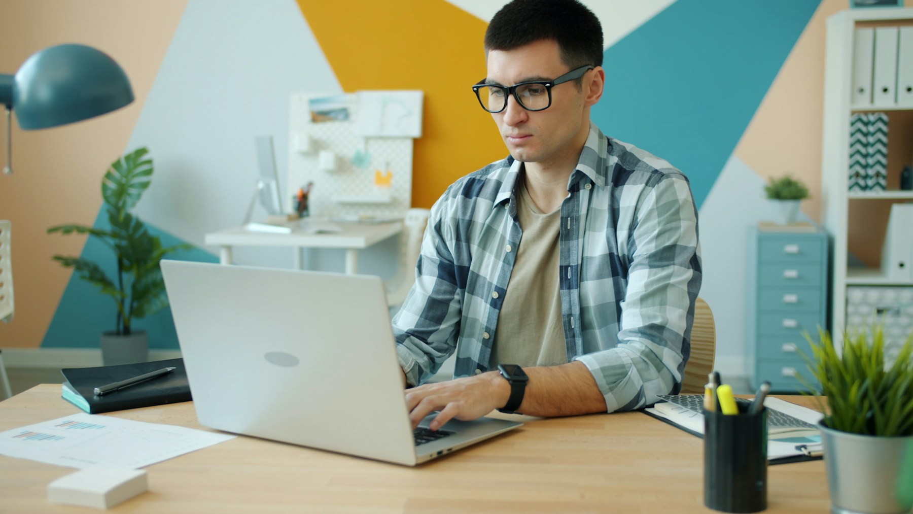 Man wearing glasses working on a laptop at a home desk, the everyday screen use blue light glasses are sold for