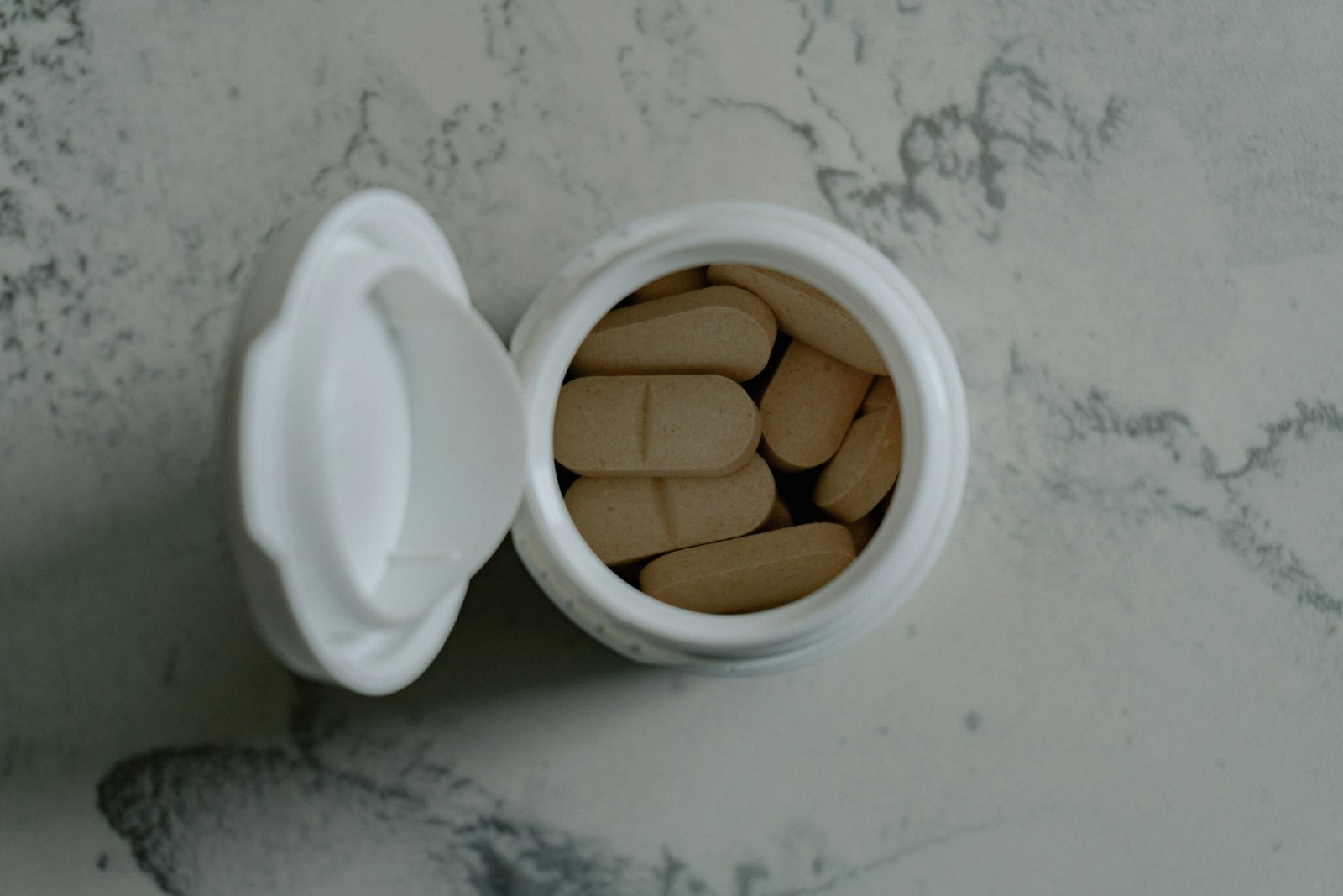 An open pot of supplement tablets on a marble worktop - the daily habit behind the question of whether collagen supplements work