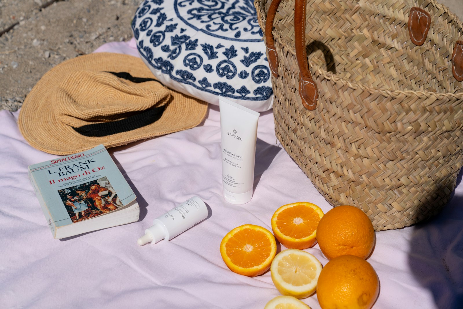 Sun cream, a straw hat and sliced oranges on a beach towel - sunscreen and vitamin C do more for collagen than a sachet
