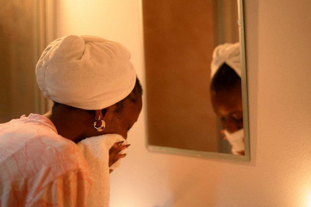 Woman drying her face with a towel in front of a bathroom mirror in the morning