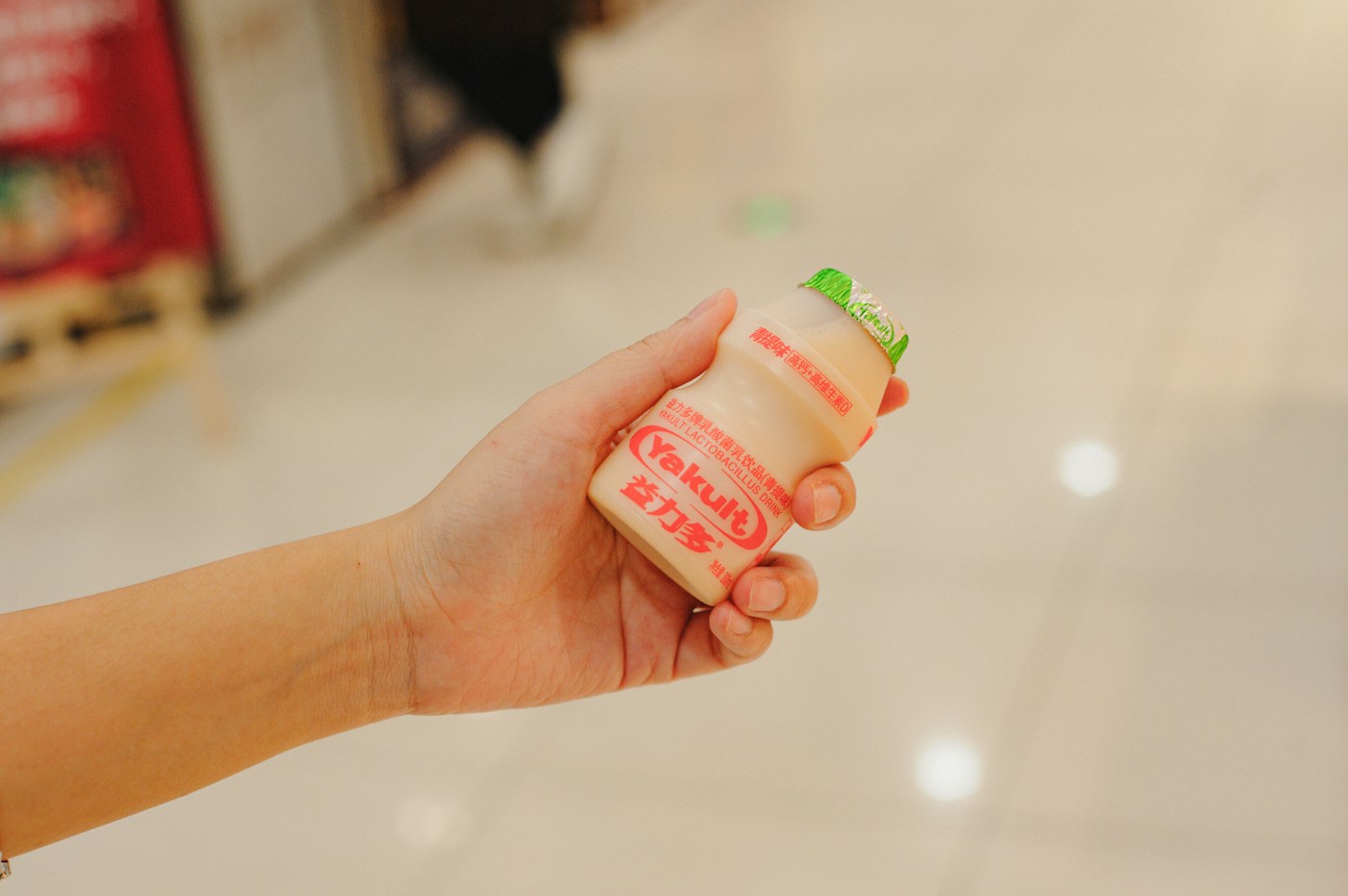 Hand holding a small bottle of Yakult in a supermarket - a few quid a week versus £150 for a 12-week course of Symprove