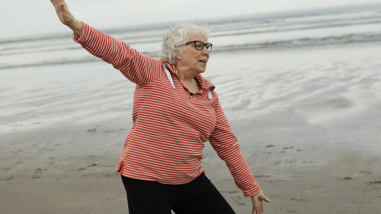 Older woman doing a tai chi balance exercise on a beach, a well-evidenced alternative for people wondering if vibration plates work for falls