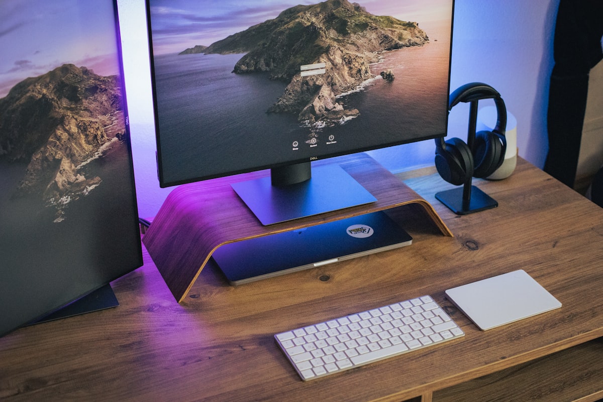 A dual monitor setup on a wooden desk with a laptop on a riser