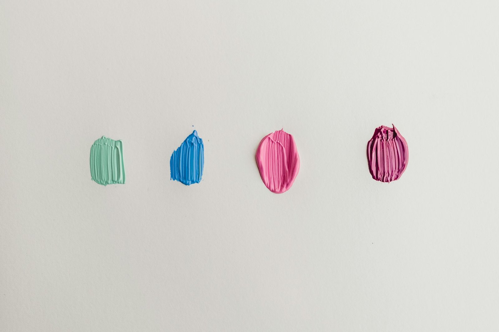 Four paint tester swatches in mint green, blue and pink on a white wall