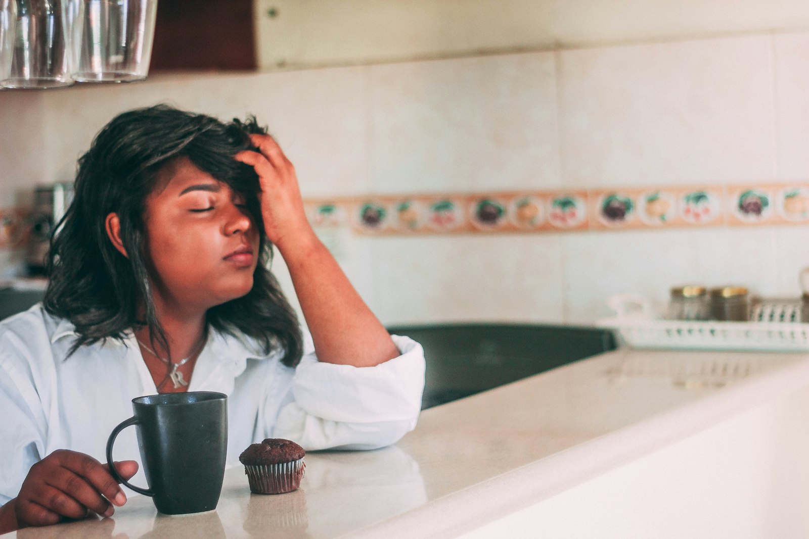 A tired woman resting her head on her hand at a kitchen counter with a mug of coffee