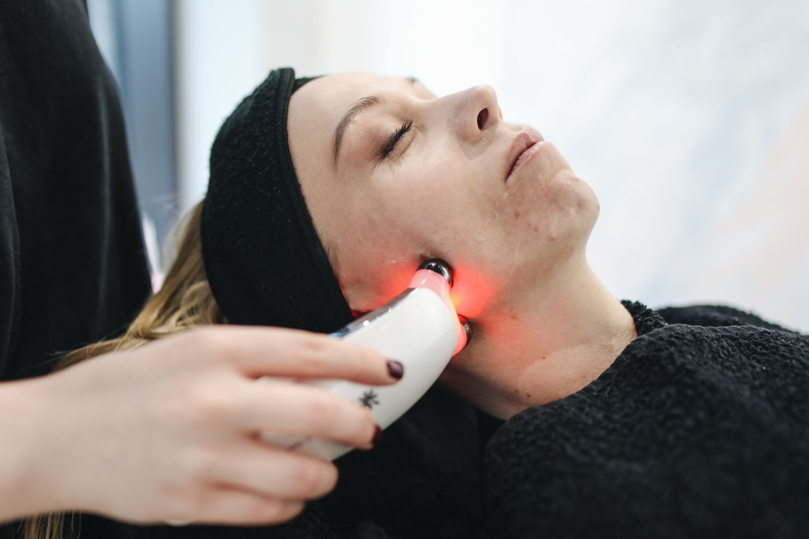 Woman receiving a red light facial treatment in a clinic, the higher-powered version of a home LED face mask