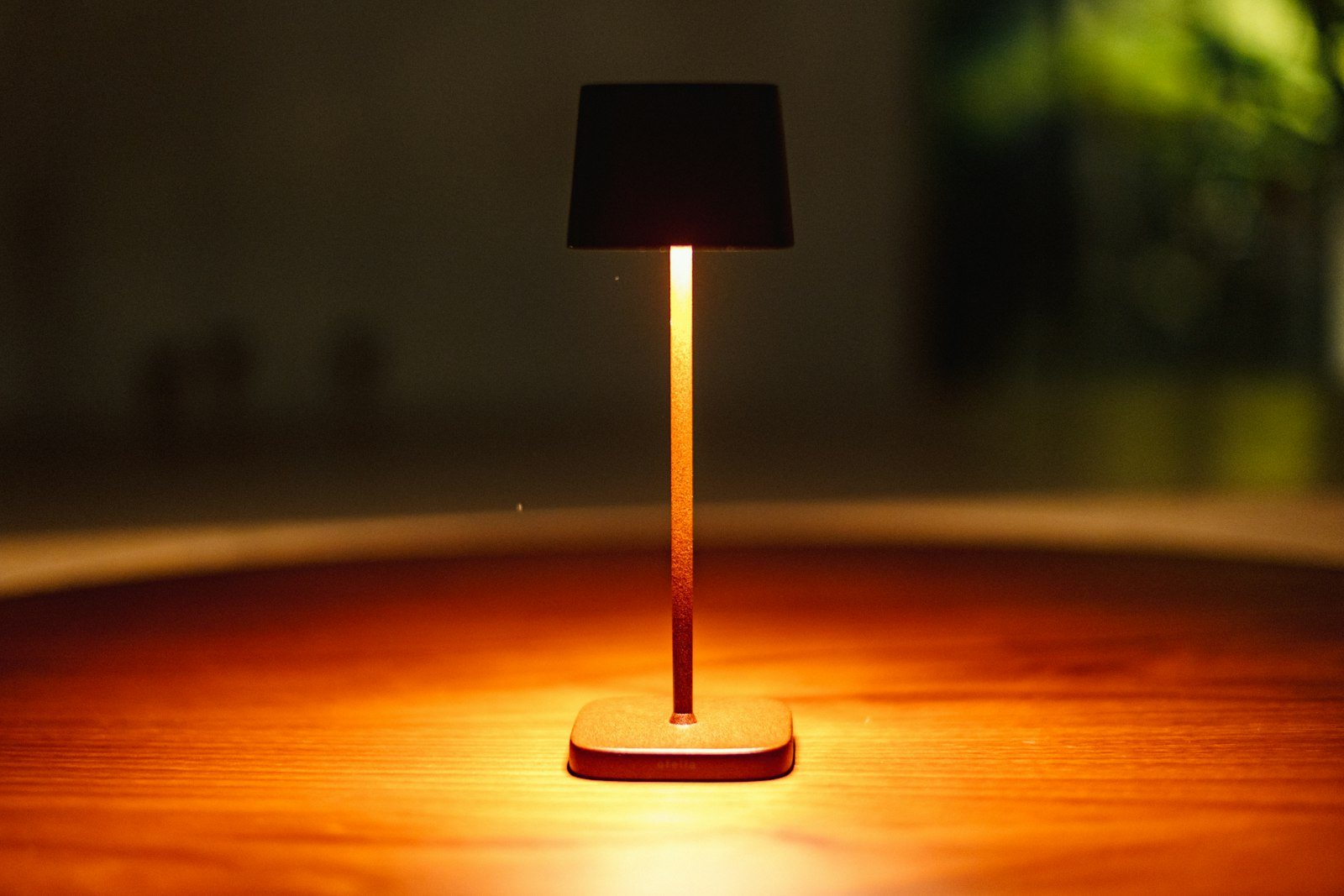 A small rechargeable cordless table lamp glowing on a wooden table