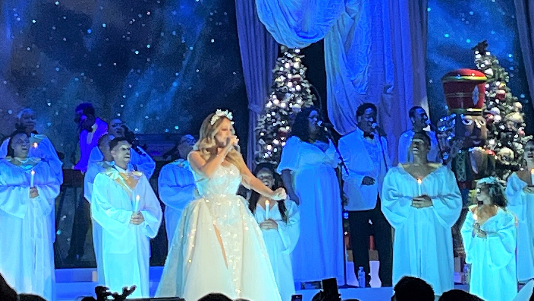 Mariah Carey performing a Christmas show in a white gown with a gospel choir behind her - the format on offer when Mariah Carey UK tour 2026 tickets go on sale