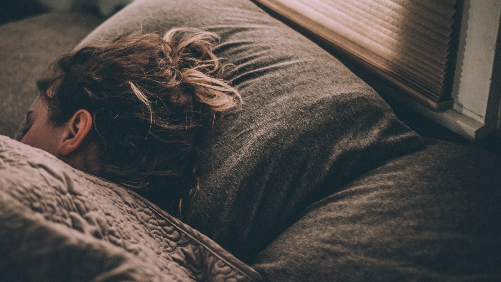 Woman asleep under blankets in morning light - CBT for insomnia outperforms melatonin gummies for adults who struggle to drop off