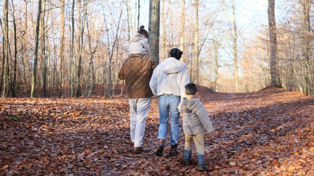 Family walking along a woodland path covered in autumn leaves during October half term breaks 2026