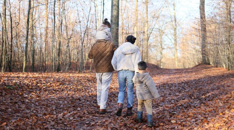 Family walking along a woodland path covered in autumn leaves during October half term breaks 2026