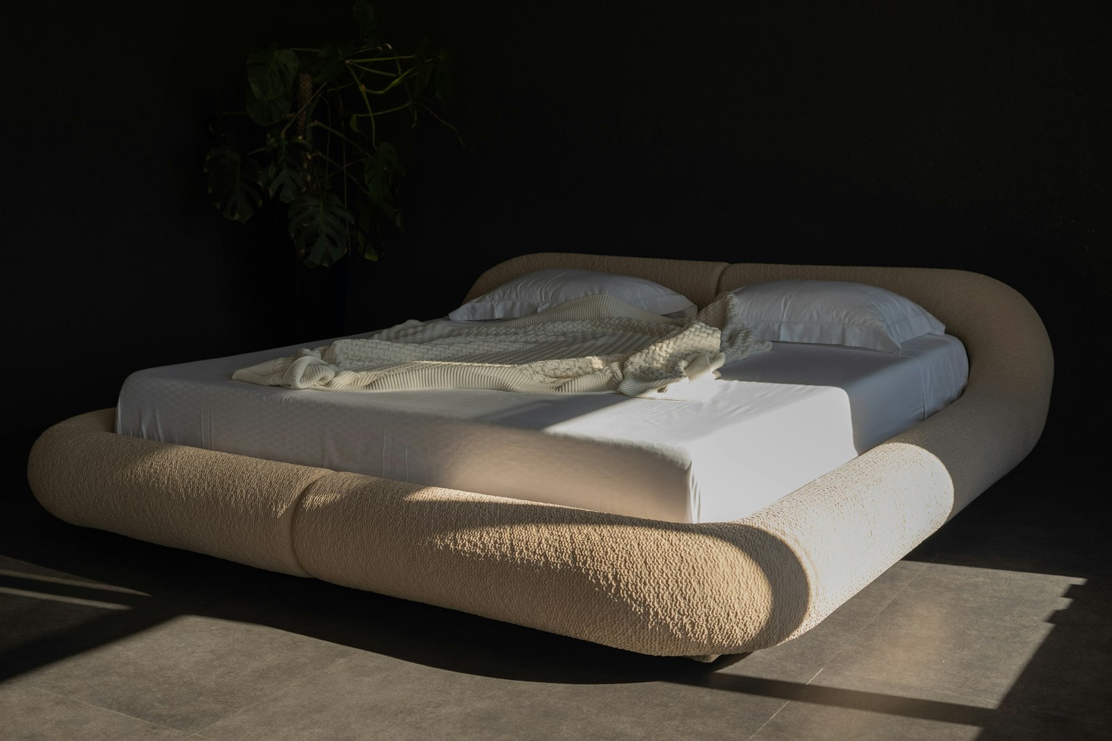 Sculptural curved upholstered bed with a rounded headboard in a dark bedroom
