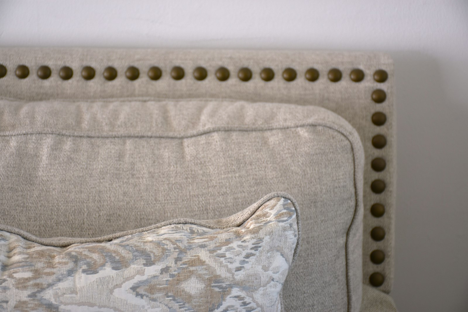 Close-up of a linen upholstered headboard with brass nailhead trim
