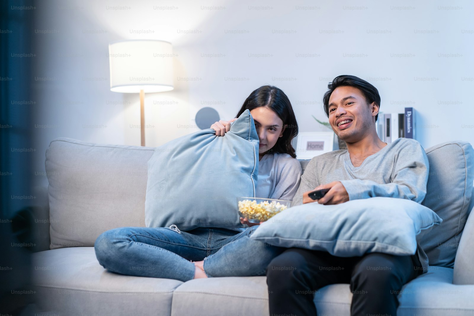 Couple on a sofa watching television with popcorn on a weekday evening