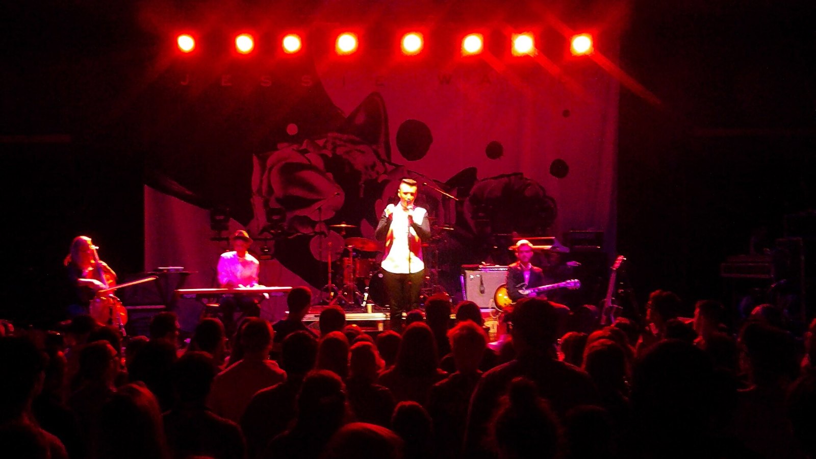 Sam Smith singing with a band under red stage lights at a small theatre show