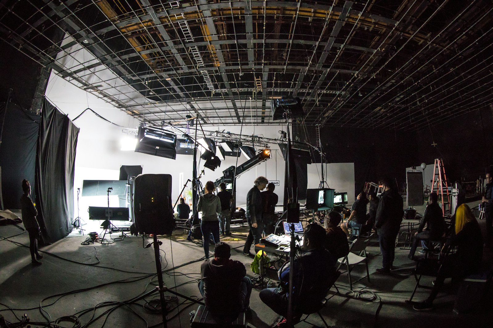 A television crew on a large studio floor under lighting rigs