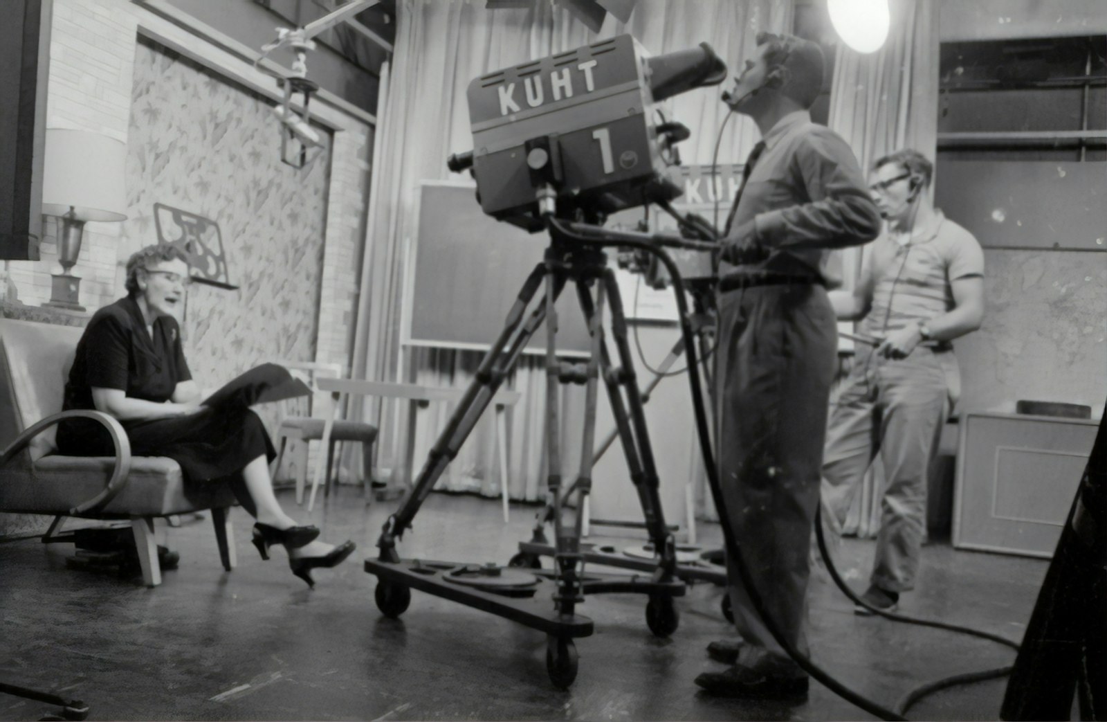 Black and white photograph of a live television studio with a camera operator and presenter