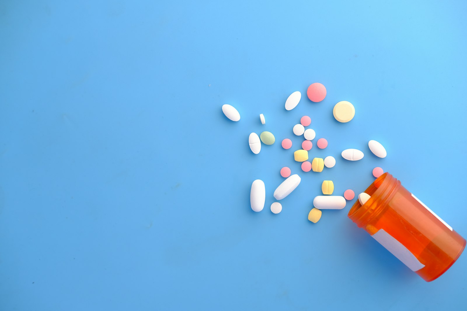 Assorted tablets and capsules spilling from an orange bottle, illustrating the choice of vitamin D supplement in autumn