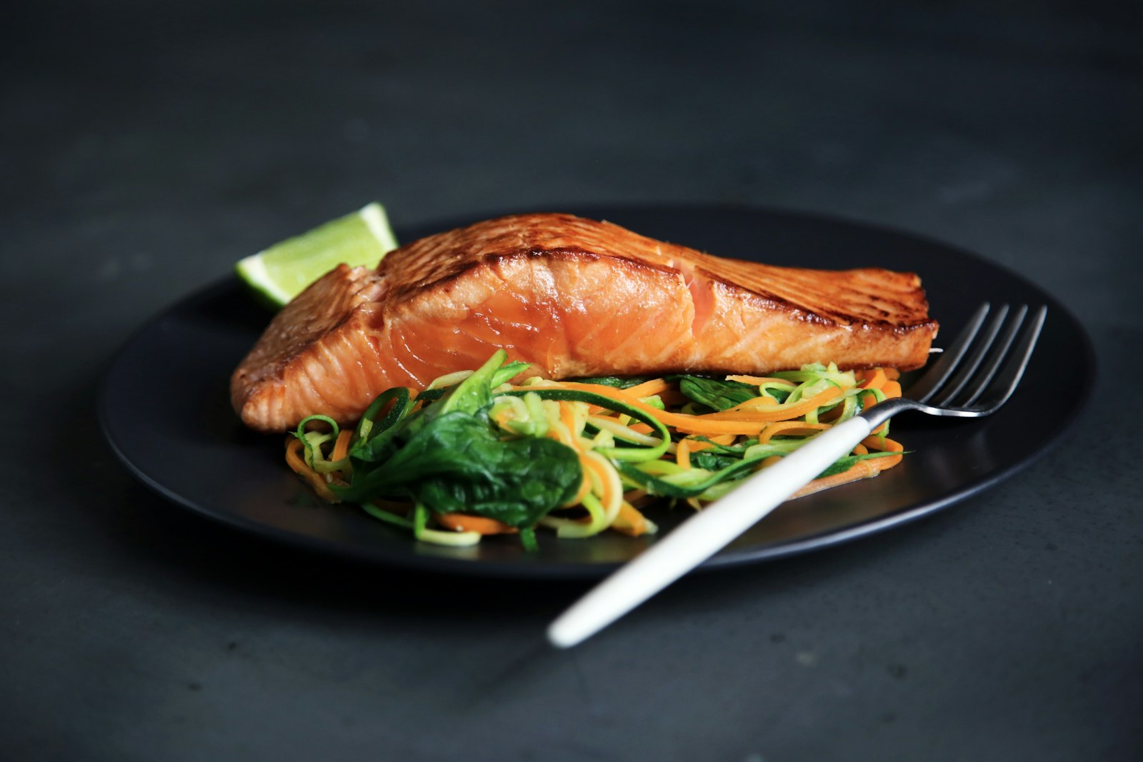 Grilled salmon with courgette ribbons and spinach on a dark plate, a food source alongside a vitamin D supplement in autumn