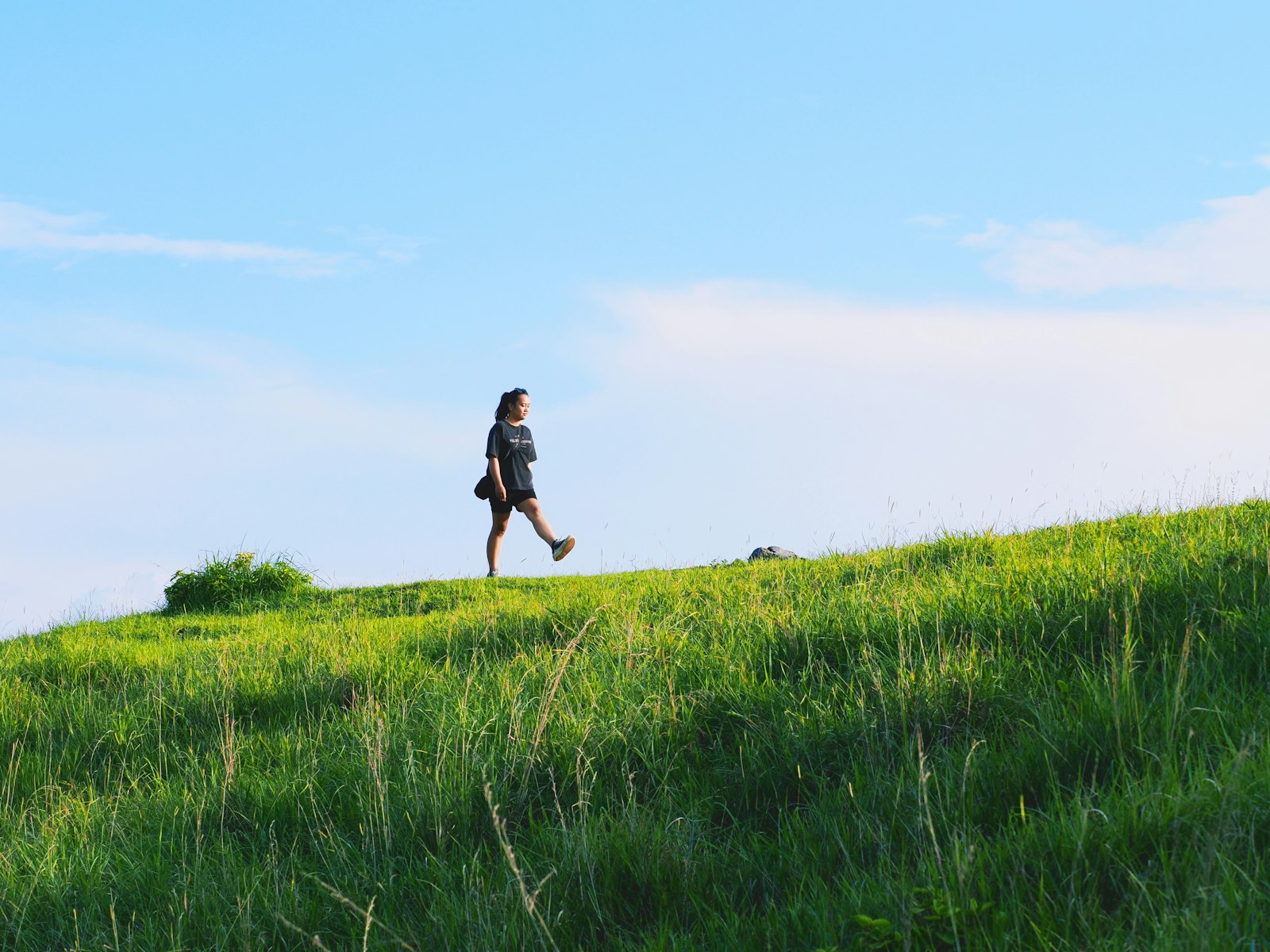 Woman doing weighted vest walking up a grassy hill on a clear day