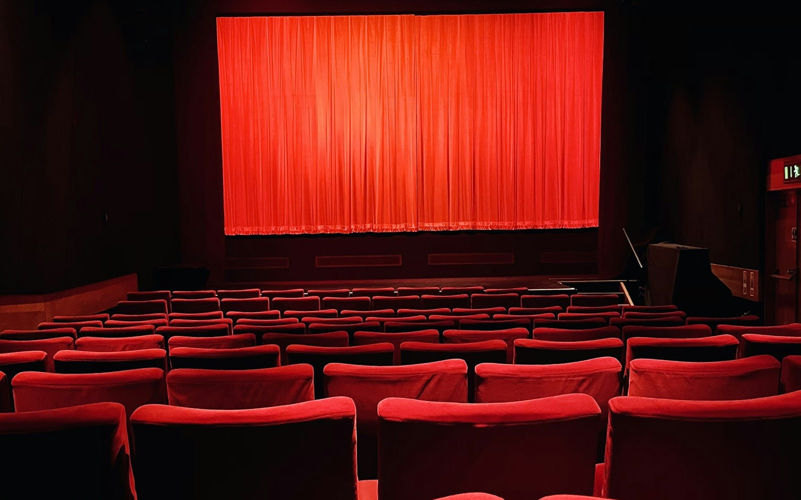 Rows of red theatre seats facing a closed curtain before a performance