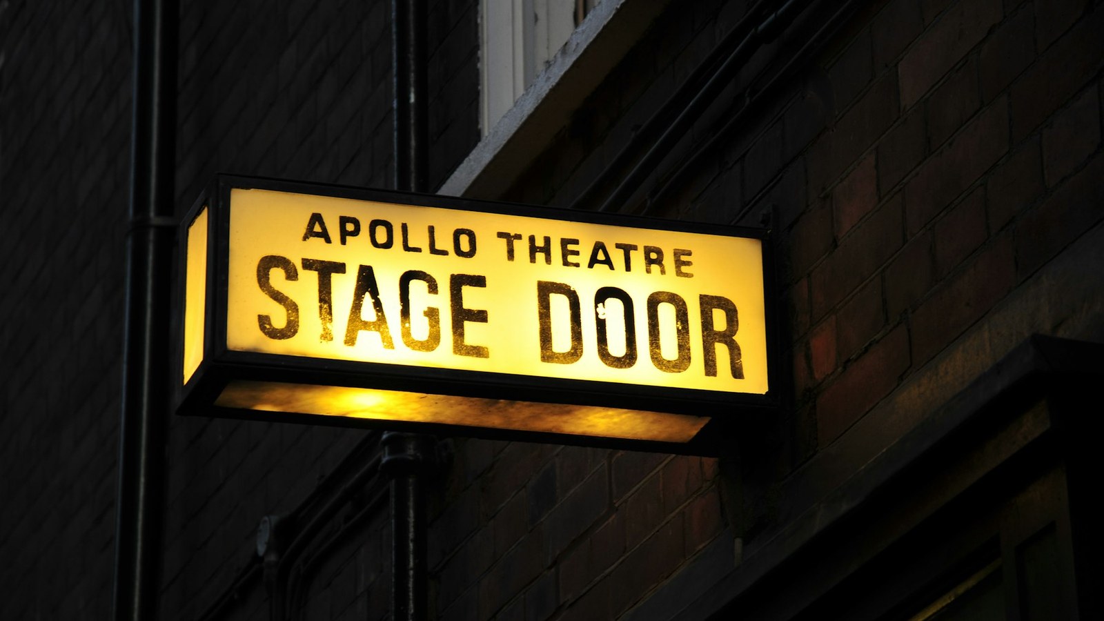 Illuminated stage door sign outside a London theatre at night