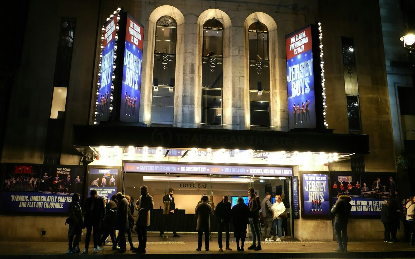 Audience gathering outside a West End theatre entrance at night