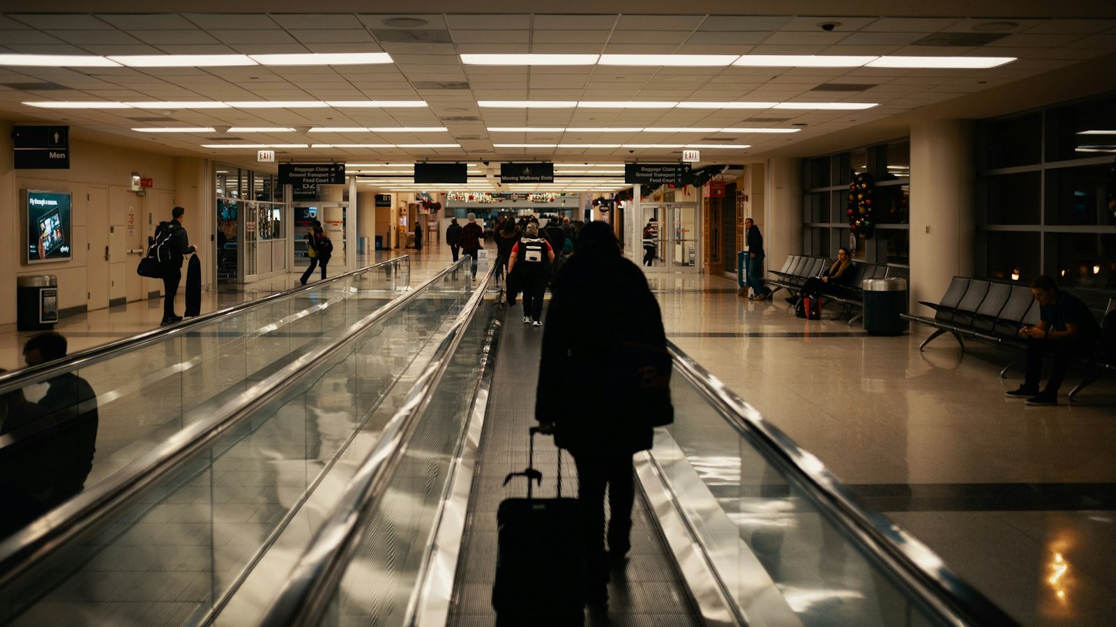 Passenger with a wheeled bag walking along a travelator in an airport departures terminal
