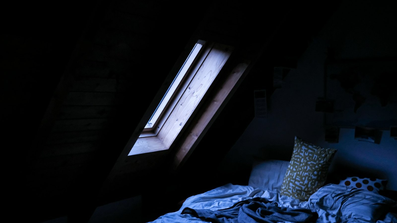 Dark attic bedroom with a rumpled bed, the sort of room where a late coffee shows up as lost sleep