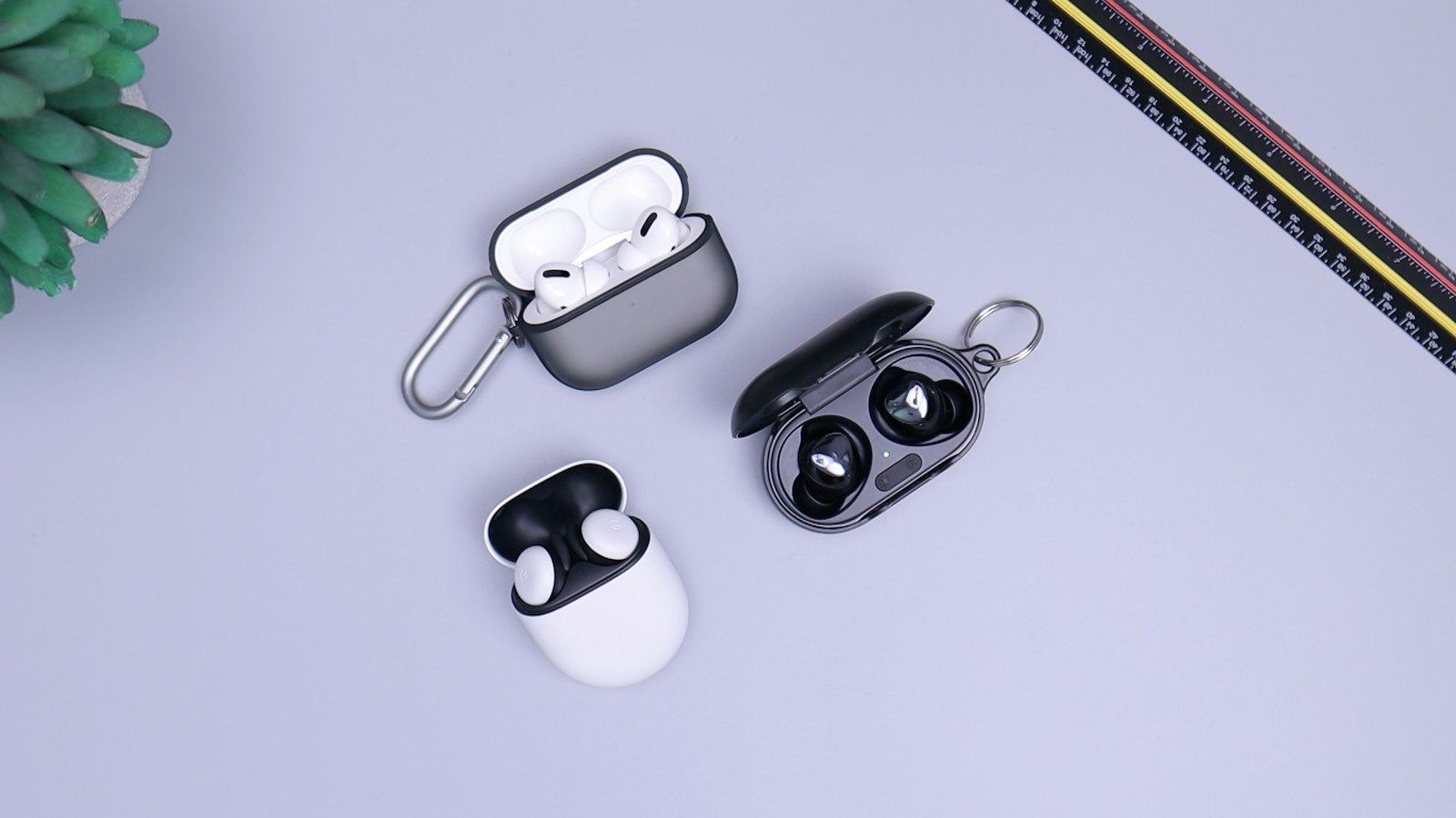 Three pairs of true wireless earbuds in open charging cases on a pale desk