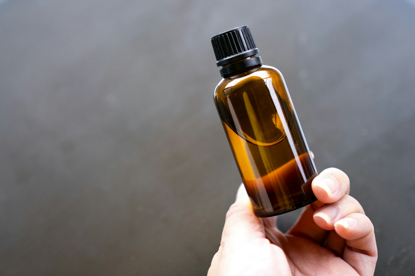 Hand holding a small bottle of essential oil, the form in which rosemary oil for hair growth is usually sold
