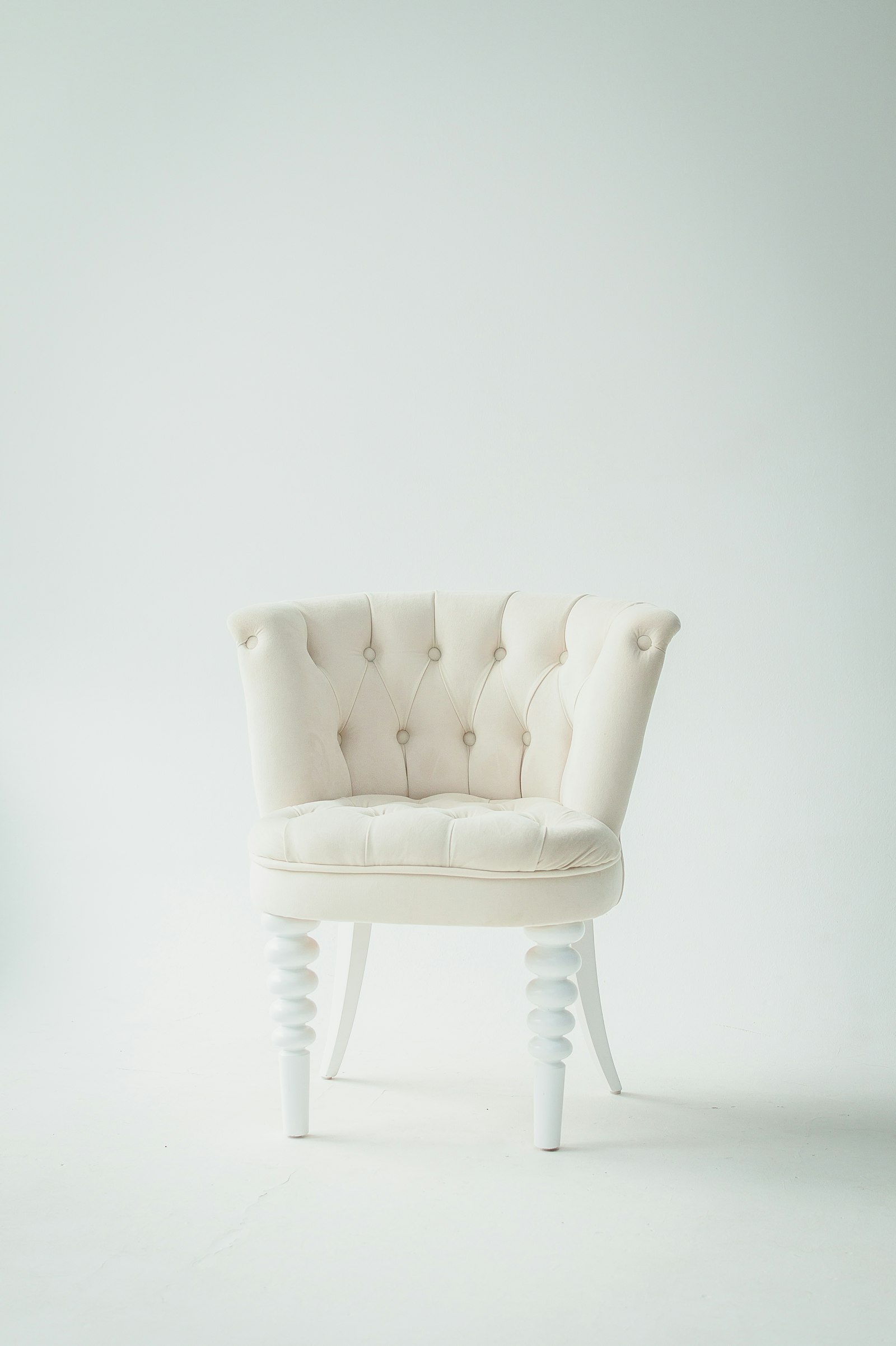 A cream tufted tub chair with turned white legs against a plain wall, an example of a sculptural accent chair