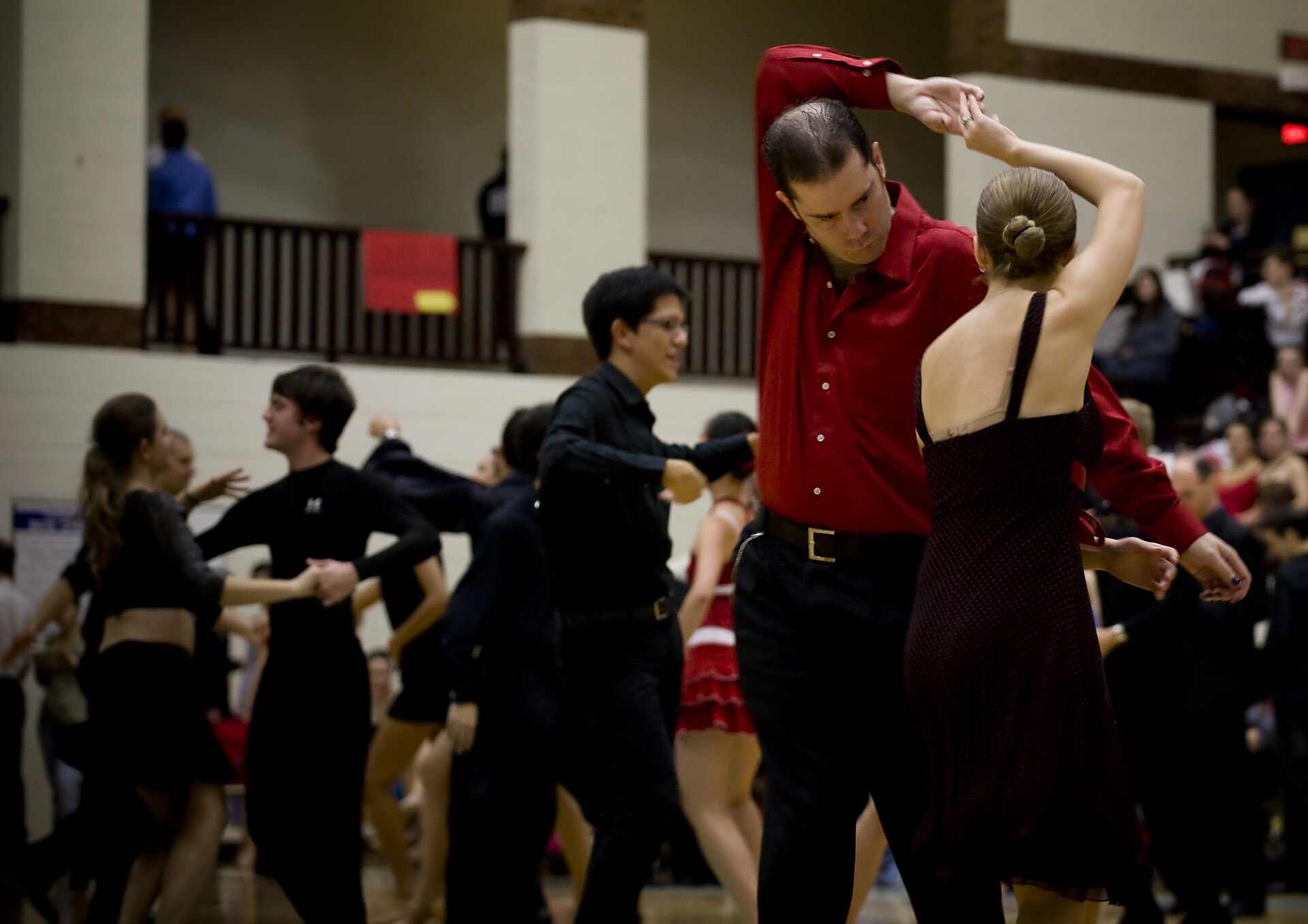 Ballroom dancers mid-routine on a wooden floor in front of a crowd