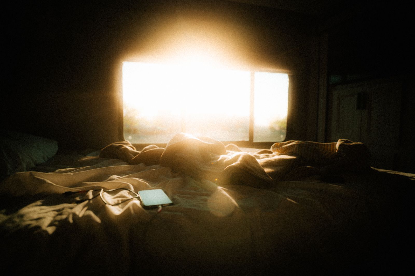 Early sunlight flooding a bedroom window over an unmade bed, the effect a sunrise alarm clock tries to recreate on dark mornings